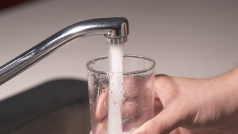 a water tap is turned on and a glass of water is filled