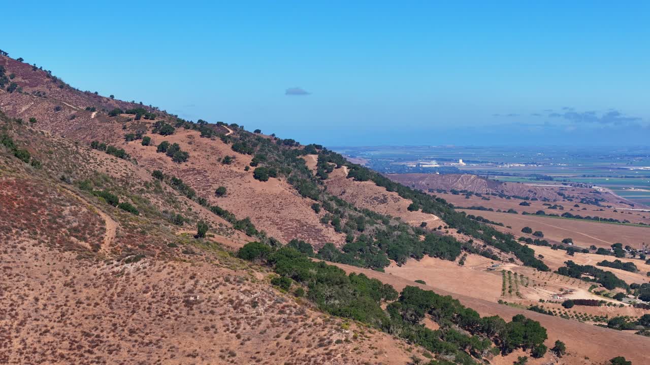 Dry mountain slope and green valley farmland under blue California sky in Salinas Valley