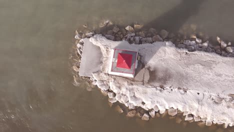 A-red-roofed-lighthouse-on-snowy-pier-in-Southampton,-winter-season,-calm-water,-aerial-view