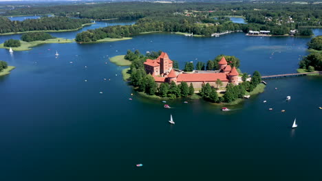 aerial: high altitude rotating shot of trakai castle with boats and yachts circling on lake around the trakai castle island with forest and trees visible in the background