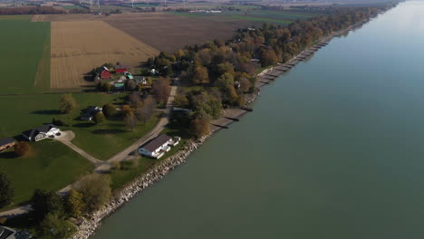 aerial parallax above calm farmland houses on edge of coastal zone or lake