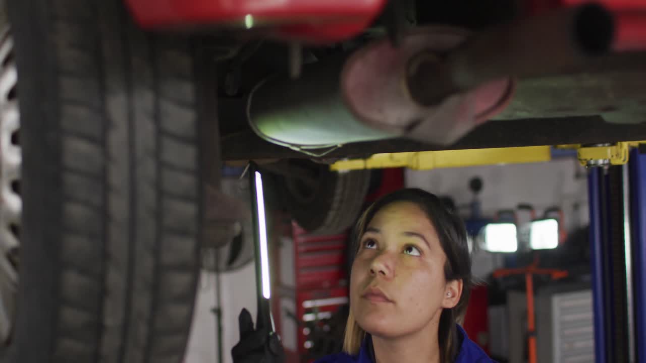 mecánica femenina usando una lámpara led y trabajando debajo de un automóvil en una estación de servicio de automóviles