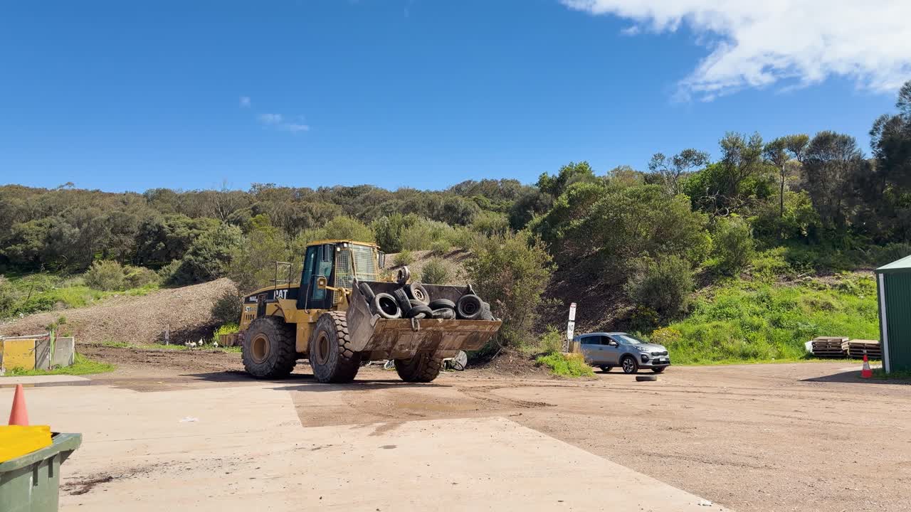 A tractor transports discarded tires at a rural waste management site under clear blue skies