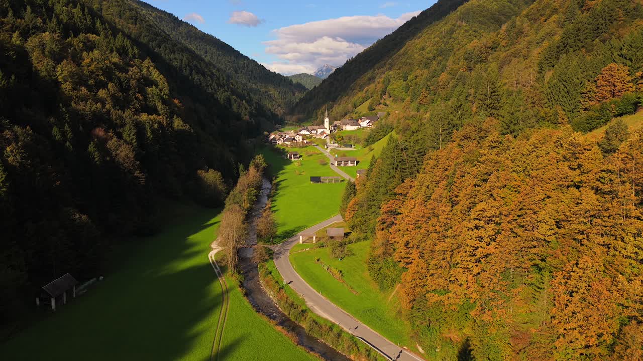 Autumn aerial reveals Zali Log village surrounded by forested hills and distant mountains in soft light, into valley