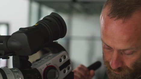 Close-Up-Of-Male-Film-Camera-Operator-Looking-Through-Eyepiece-Shooting-Movie-Or-Video-In-Studio