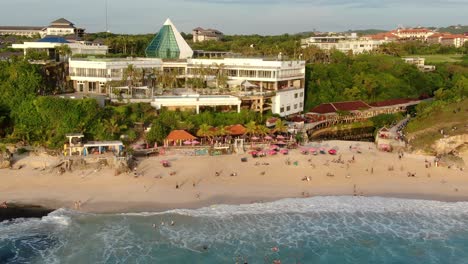 Dreamland-Beach-is-located-in-ULUWATU,-Bali,-and-features-a-cliff-overlooking-a-turquoise-translucent-sea,-a-local-cafe-restaurant,-a-swimming-pool,-and-a-blue-sky-with-surf-waves