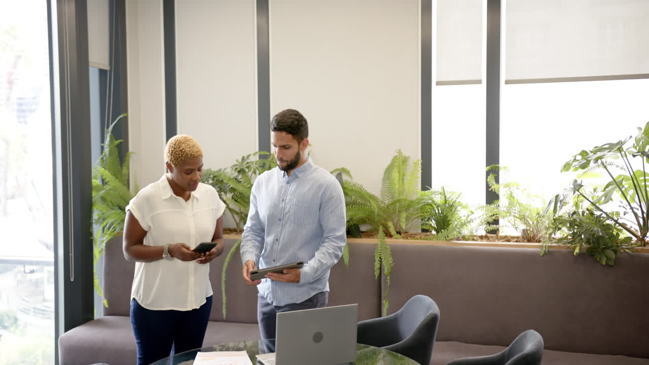 Discussing work, diverse colleagues using smartphone and tablet in modern office setting