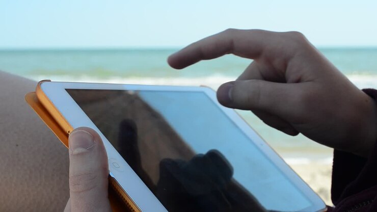 Il tablet nelle mani della ragazza sulla spiaggia. Lavoro sul tablet. Riprese sulla spiaggia.