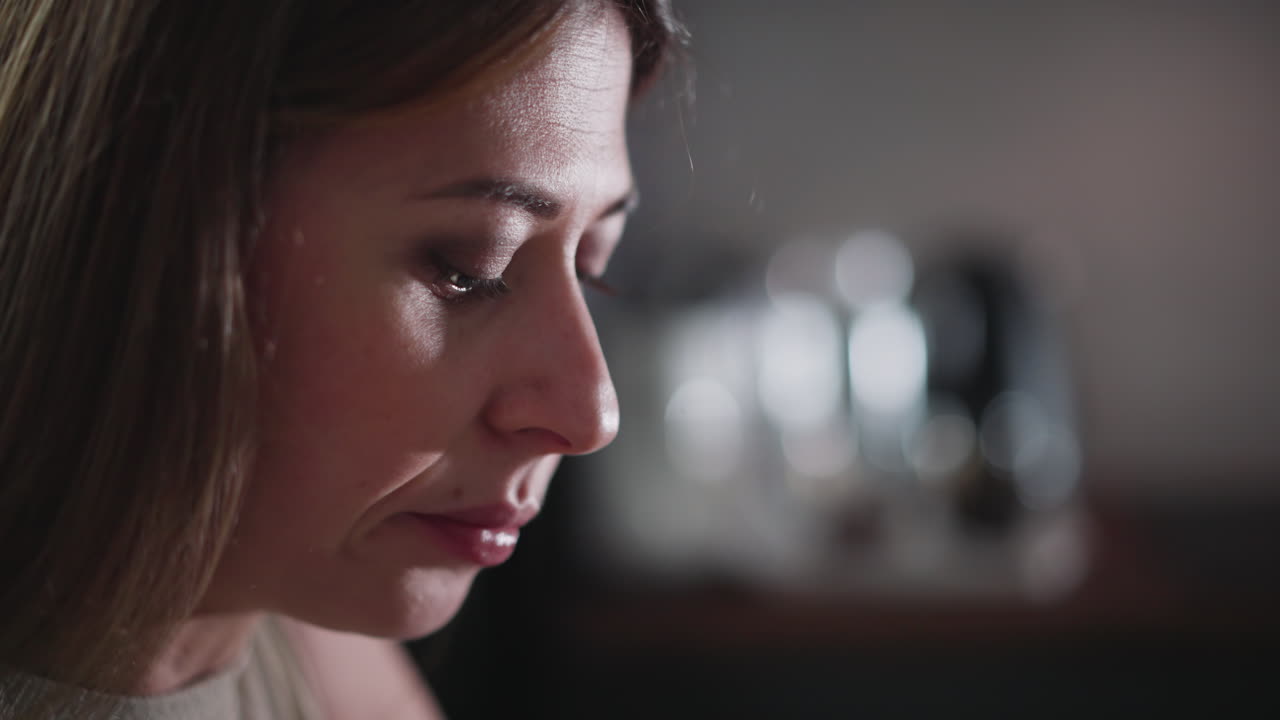 Close up side view of young lady eating with serious expression, featuring soft bokeh lights in blurred background, wearing sleeveless top indoors, showing focus on food
