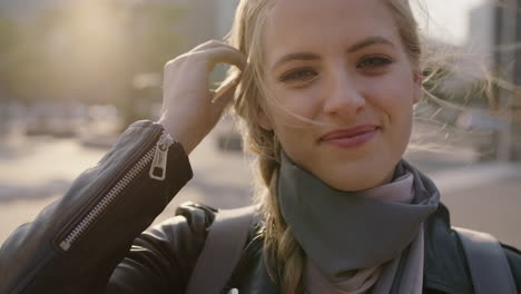 slow motion portrait of cute young blonde woman smiling at camera running hand through hair enjoying sunset in urban city commuting