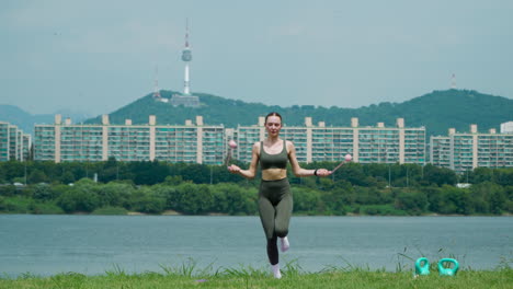 Fit-Sporty-Woman-Exercising-with-Cordless-Jump-Rope-Jumping-on-One-and-Both-Legs-at-Han-RIver-Park-With-Iconic-N-Seoul-Namsan-Tower-in-Backdrop
