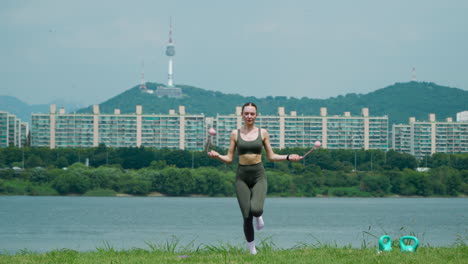 한강 공원에서 코드리스 점프 로프로 운동하는 건강한 스포츠 여성이 한강 공원에서 한강 토너를 배경으로 하고 있다