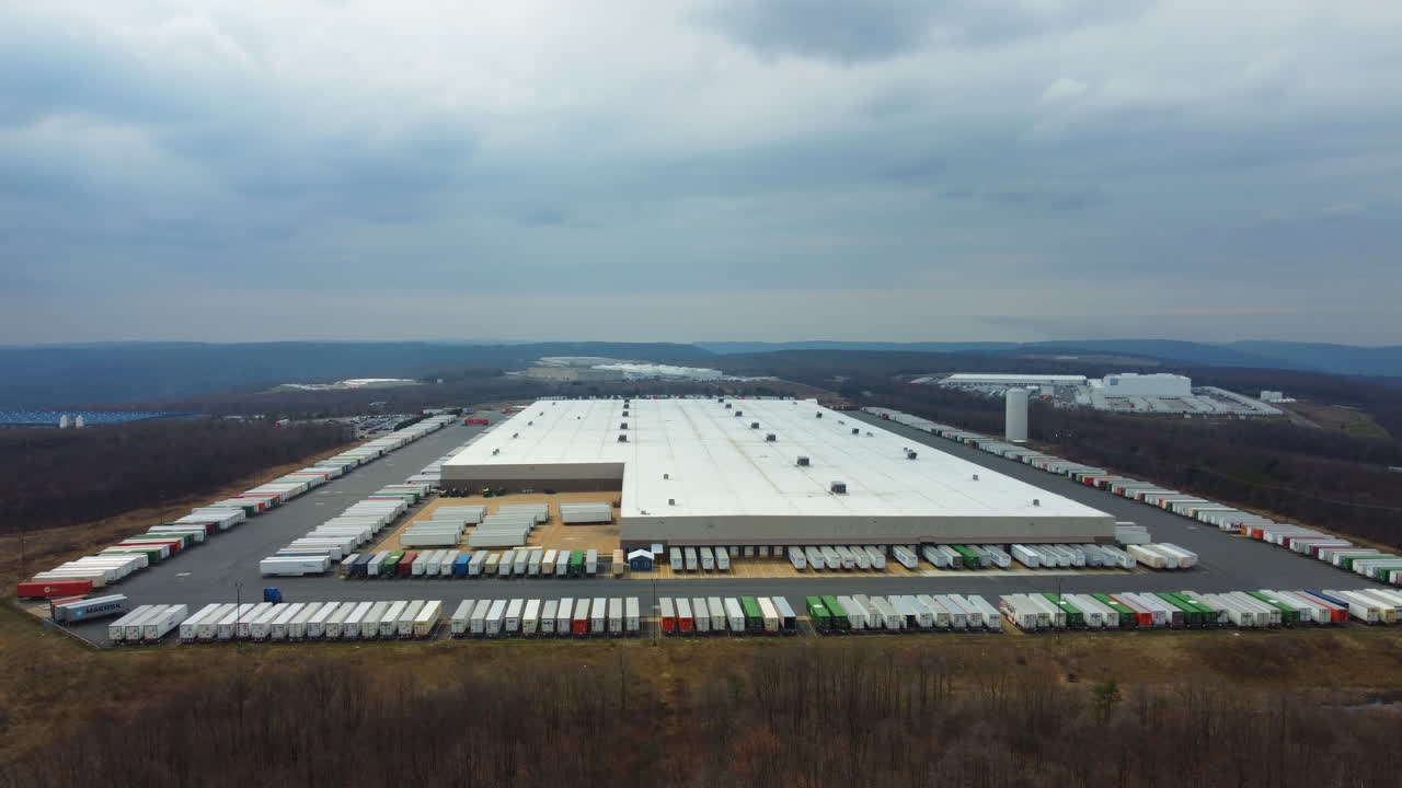 A drone pan moves toward a shipping center in Schuylkill County, revealing hundreds of containers neatly arranged with the soft blue mountains rising in the distance industry meets natural beauty.