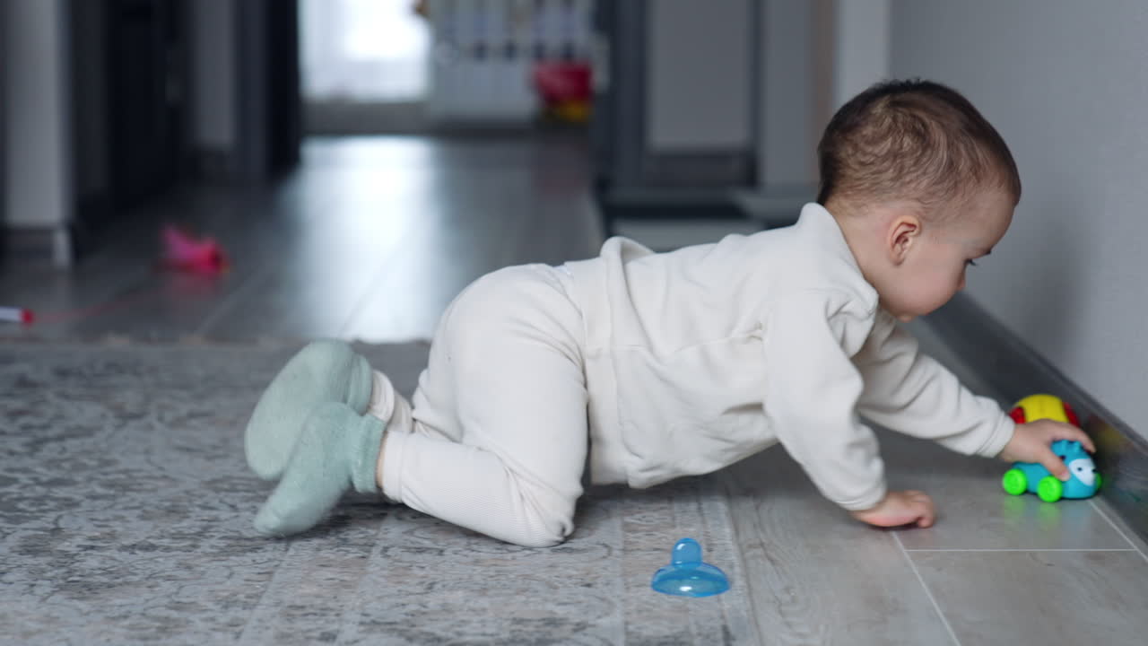 One year old toddler playing with toys. Kid crawls by the floor moving a little car. Blurred backdrop.