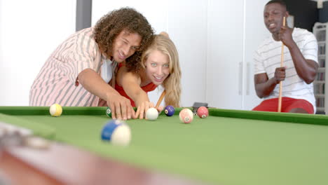 biracial man teaches young caucasian woman to play pool, with copy space