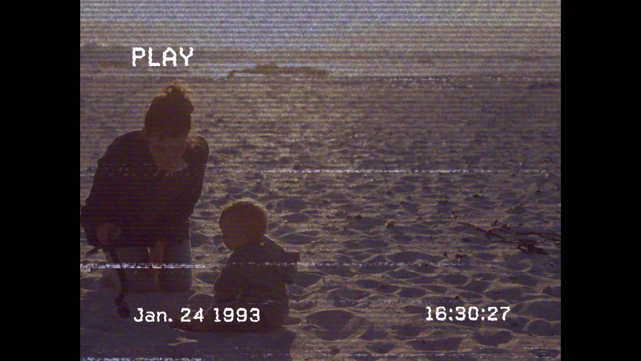 Parent crouching on beach, offering toy to baby, supporting education, tape overlays showing