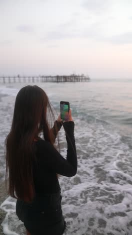 woman taking photo on the beach at sunset