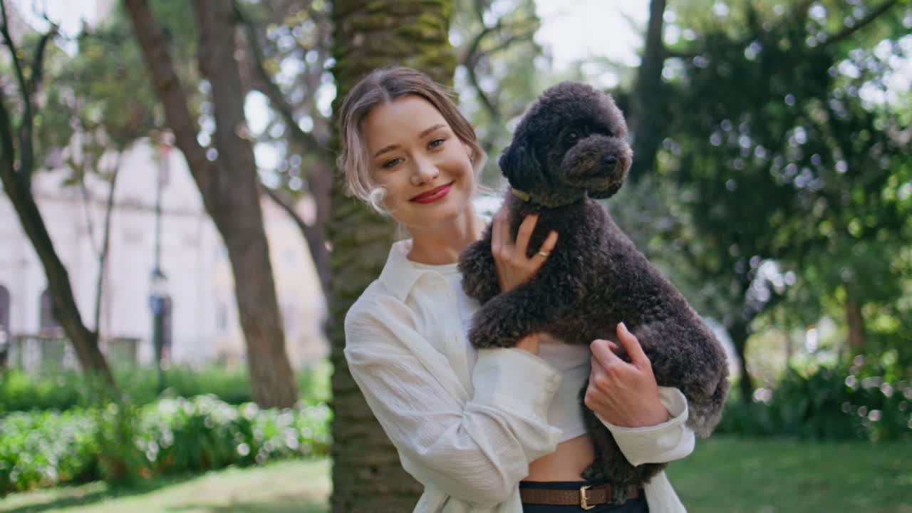 Cheerful girl posing poodle in sunny park closeup. Smiling woman cuddling pet