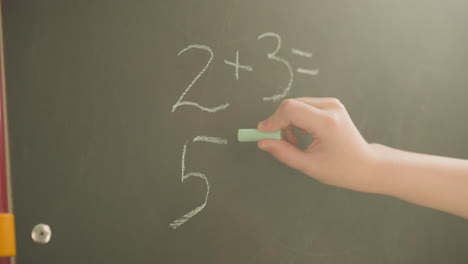 schoolgirl writes mathematical examples on blackboard