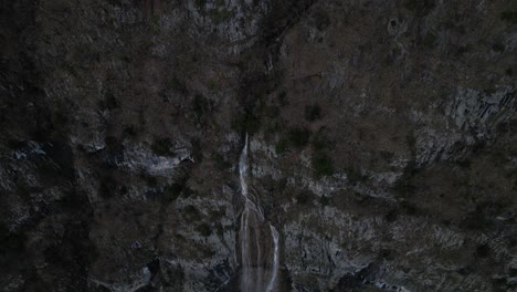 Drone-clip-showing-tall-flowing-waterfall-and-surrounding-steep-rocky-cliff-edge