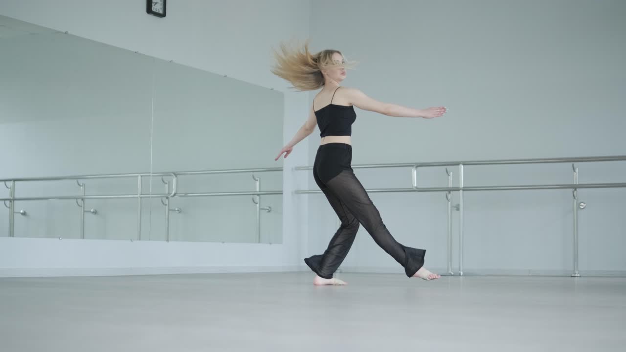 흑색 옷을 입은 소녀가 동시대를 선보이며, 여성 댄서가 하 방에서 흐르는 움직임, 몸과 손의 파동을 보여줍니다. 현대 발레 댄스 안무. 젊은 여성이 부드럽게 움직이고 있습니다.