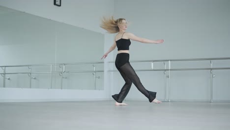 fit girl in black clothes performing contemporary. female dancer shows flowing motions, body and hands waves at white room. modern ballet dance choreography. young woman is moving smoothly