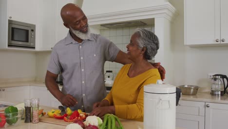 Un-Anciano-Afroamericano-Abrazando-A-Su-Esposa-Mientras-Cortaba-Verduras-En-La-Cocina-De-Casa