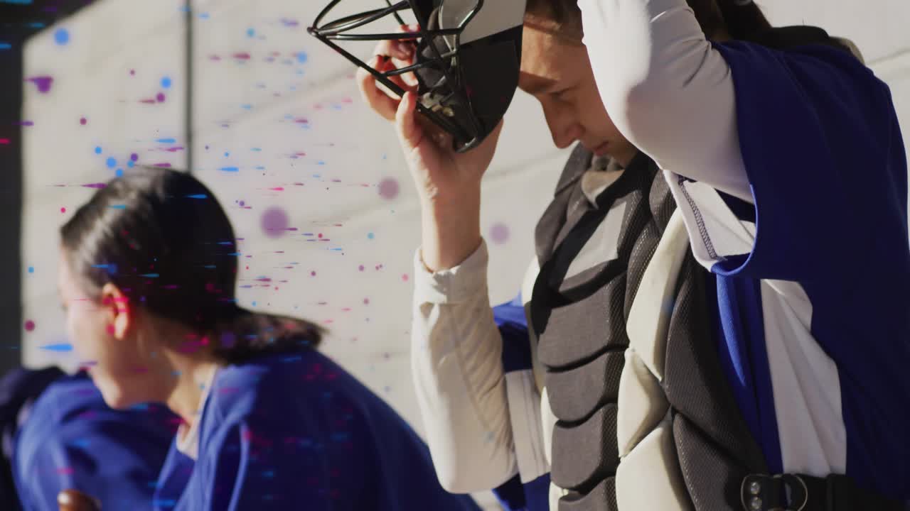 Baseball catcher reaching down gripping helmet in dugout lifting mask and securing straps pre-game