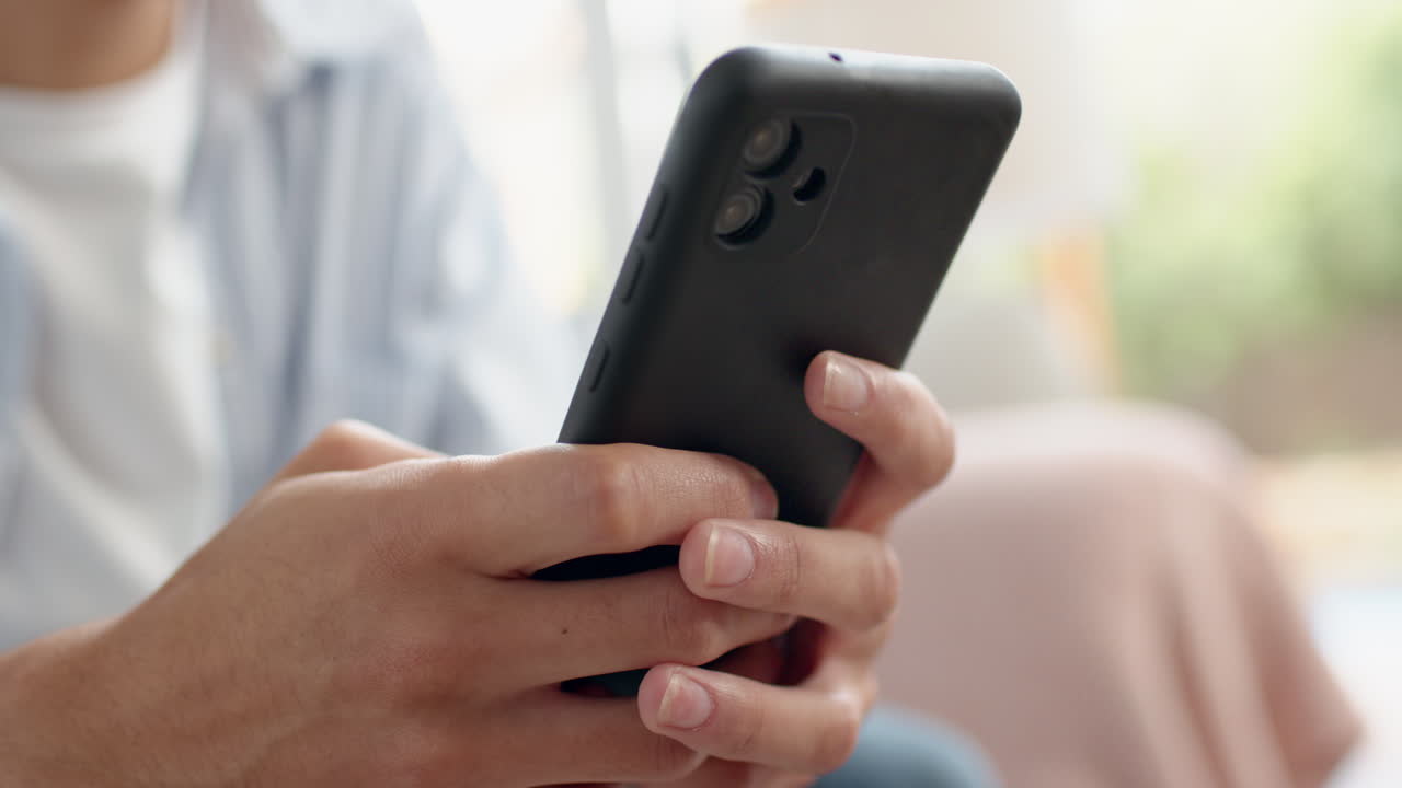 Holding smartphone, teenage boy texting and browsing at home, close-up of hands