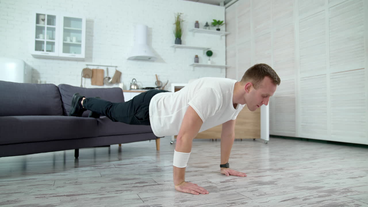 Sportive guy doing push ups at home. Young man exercising on a floor with his legs on a couch. Workout in apartment during isolation.
