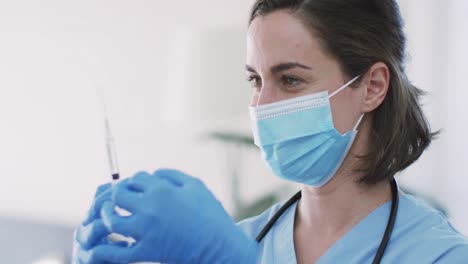 Caucasian-female-doctor-wearing-face-mask-at-home-with-vaccine