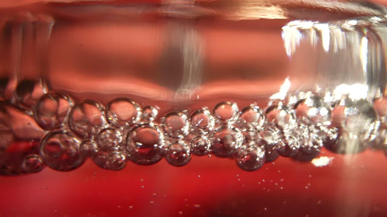 Clear bubbles Forming On The Surface Of An Alcohol Beverage In A Clear Glass, Studio Shot With Red Background.