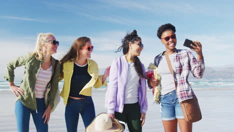 happy group of diverse female friends having fun, taking selfie with smartphone at the beach