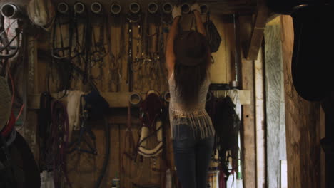 cowgirl grabs her horse riding gear off the wall of a rustic old barn-1