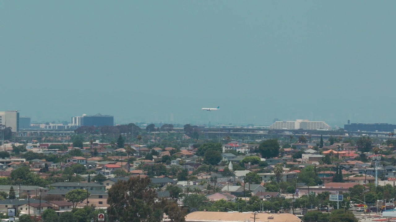 Tele-Schwenkaufnahme aus der Luft eines landenden Flugzeugs am LAX in der Ferne, gesehen von Hawthorne, Kalifornien. 4K