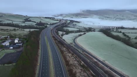 volando sobre el puente en la tranquila autopista m6 hacia colinas cubiertas de niebla al amanecer en invierno con un viaducto de piedra en la distancia