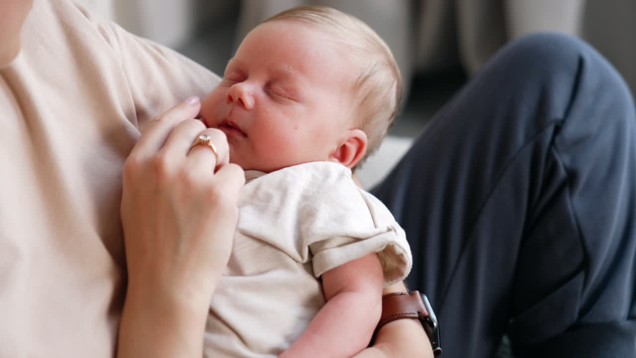 Cropped image of a mom holding her sleeping baby in hands. Mother touches her child's nose with a finger. Close up.
