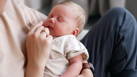 cropped image of a mom holding her sleeping baby in hands. mother touches her child's nose with a finger. close up.