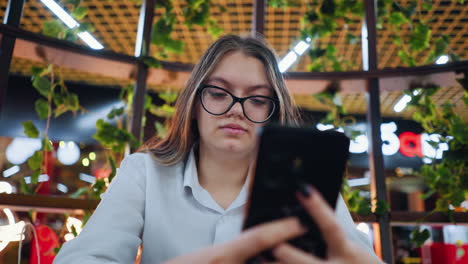 freelancer sentado en una silla de madera decorativa, hablando con el cliente por teléfono con una sonrisa sutil, en un restaurante bien decorado en un centro comercial ocupado