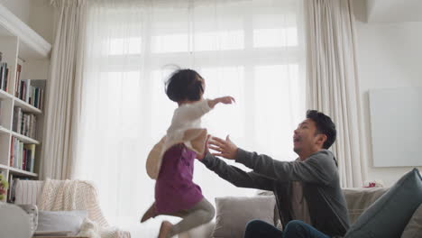 cute little asian girl jumping into fathers arms happy dad gently catching his daughter enjoying playful game with child at home 4k