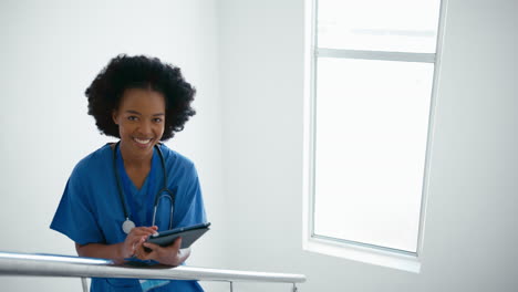 Portrait-Of-Female-Doctor-Or-Nurse-With-Digital-Tablet-Checking-Patient-Notes-On-Stairs-In-Hospital
