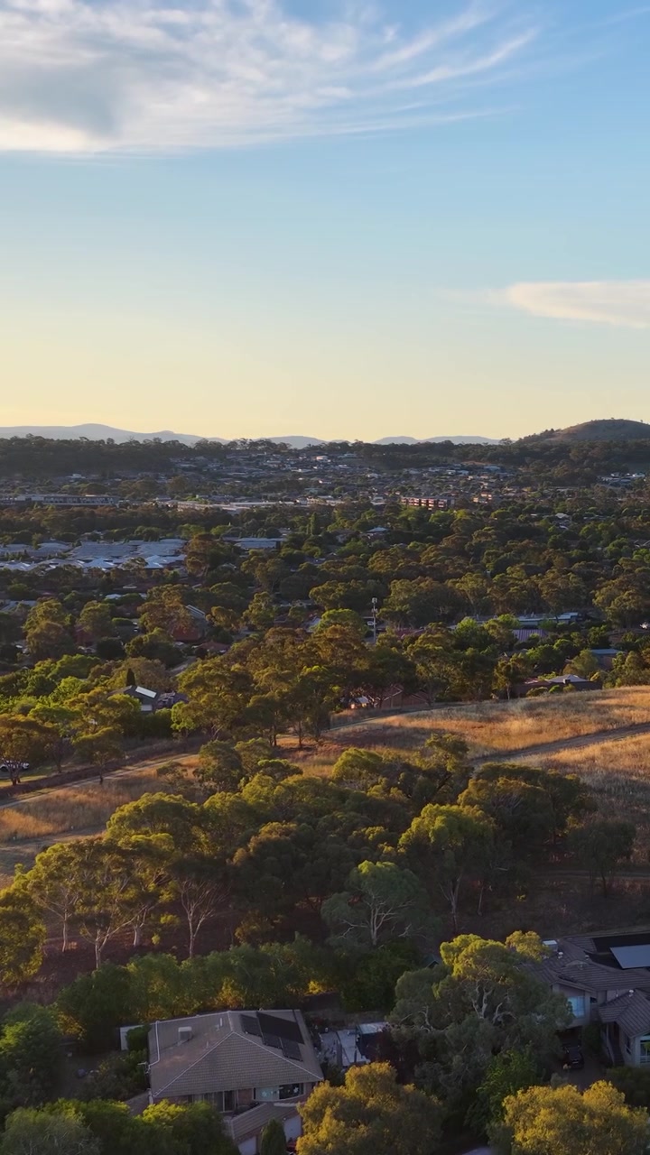 Un drone effettua una panoramica su case residenziali e un lussureggiante parco verde a Canberra durante l'ora d'oro.