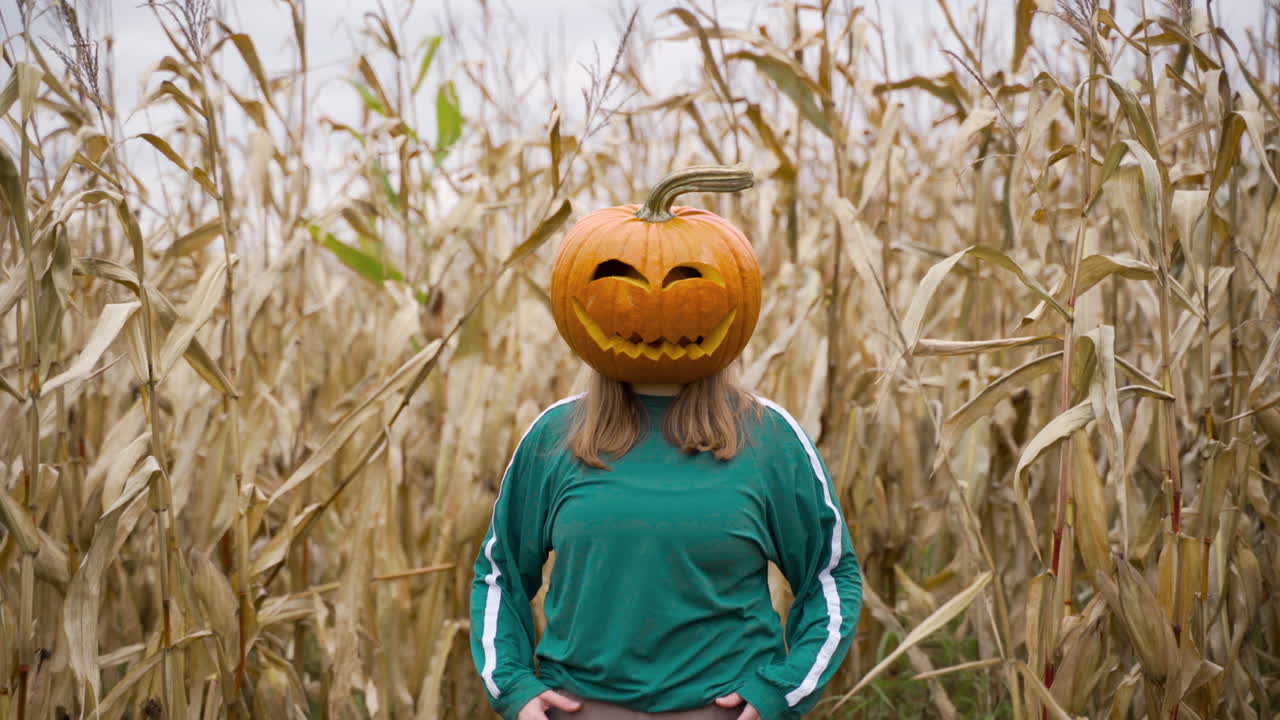 옥수수 농지에서 금발 소녀의 머리에 새겨진 할로윈 호박