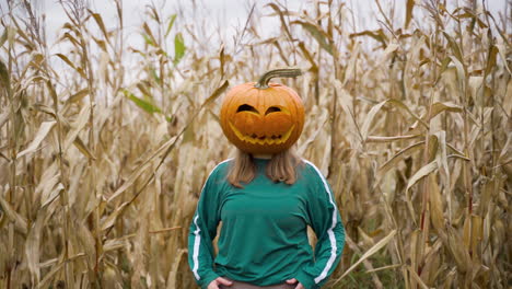 carved halloween pumpkin on the head of a blonde girl in corn farmland