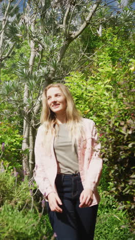 vertical video of happy caucasian woman walking in garden on sunny day