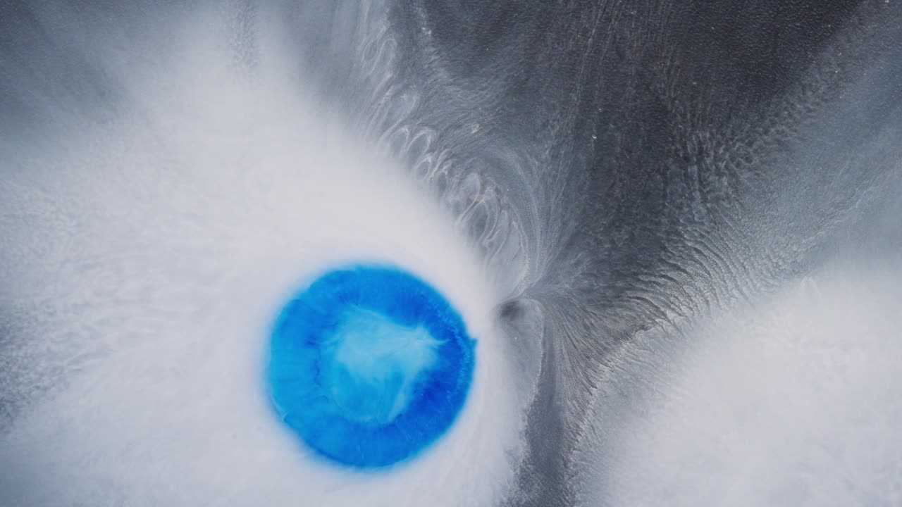 Blue ink drop creating abstract patterns in white fluid under macro lens
