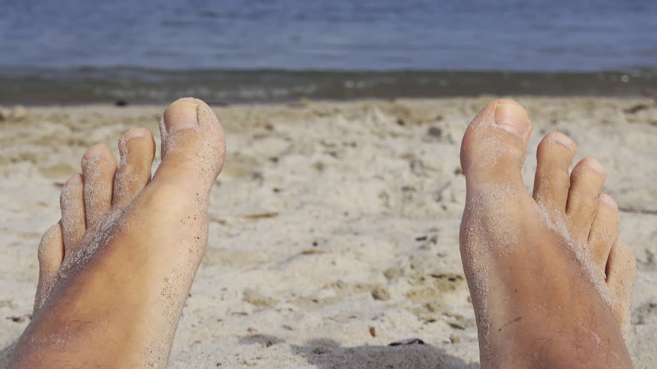 Close up of a man's wet and sandy feet on a beach with a view of the sea