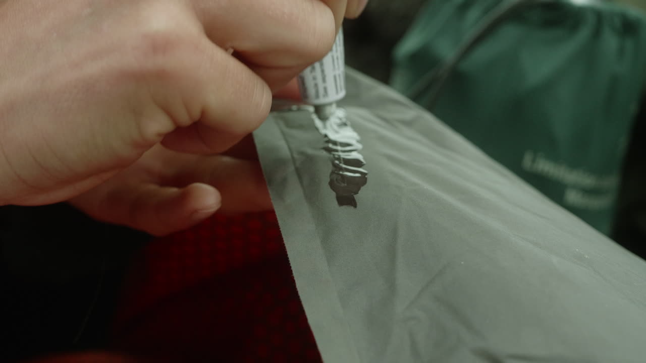 primer plano de una mujer reparando un agujero en un colchón de campamento con la ayuda de pegamento, poniendo una segunda capa