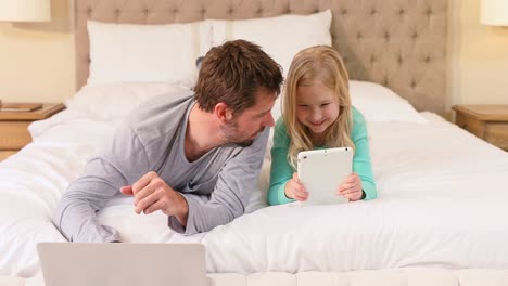 Happy-father-and-daughter-lying-on-bed-using-laptop-and-tablet-4K-4k