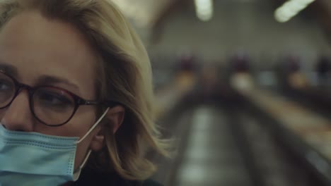 girl with eye glasses and disposable face mask riding escalator moving inside the building during the pandemic coronavirus